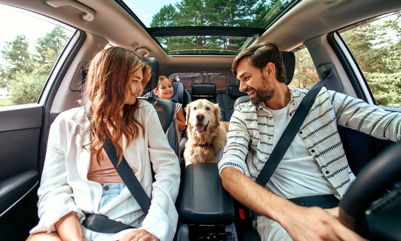 Família composta por um homem, uma mulher e uma menina dentro de carro durante uma viagem com o cachorro.